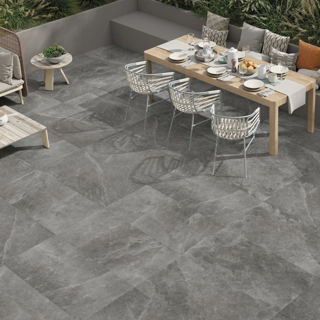 Angled ariel view of an outdoor dining area. The tiles floors are a dark stone look grey tile with veining and earthy vibe. 
