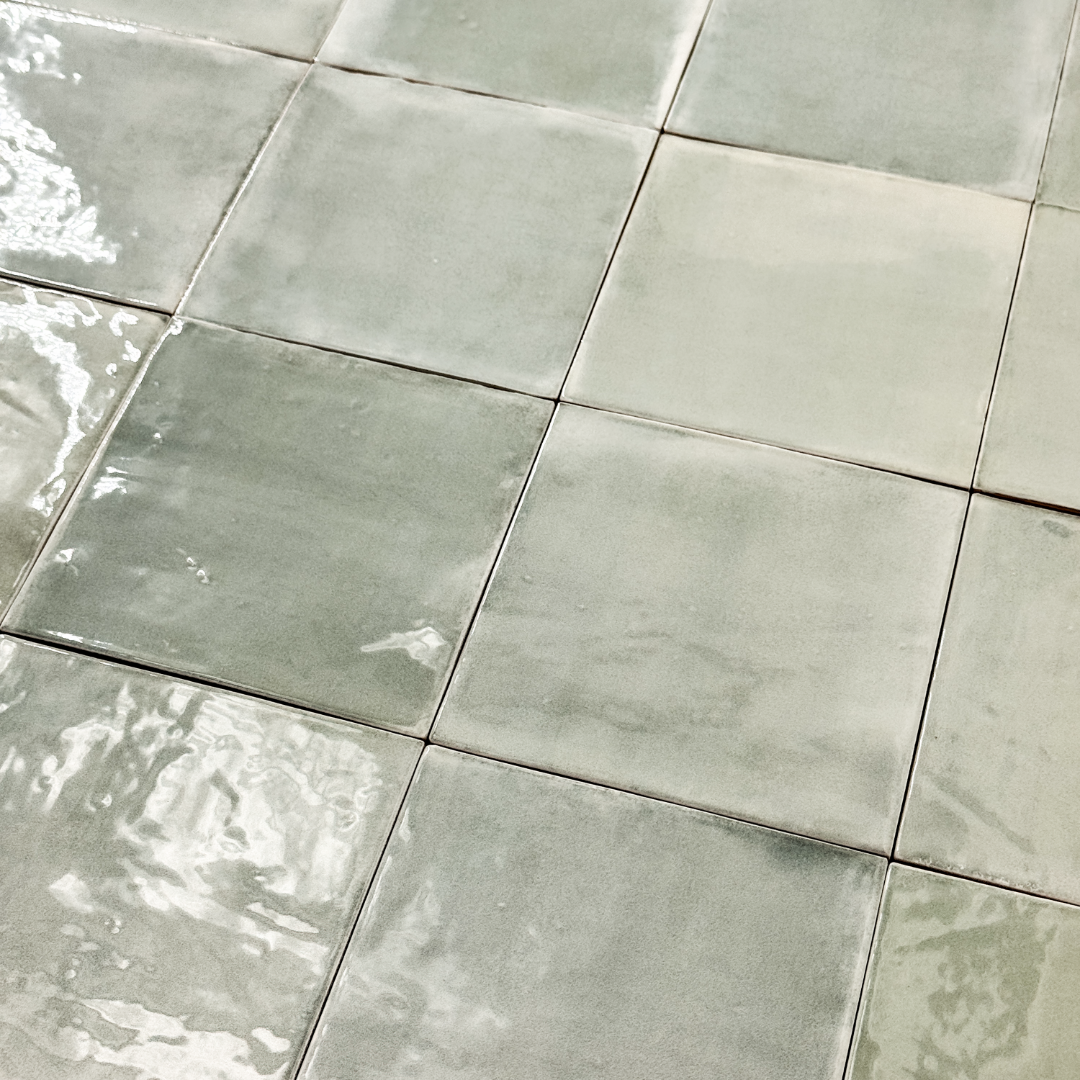 Angled close up view of a group of glossy 5x5 textured light green blue earthy zellige tiles showing the textured edges and colour variation. 