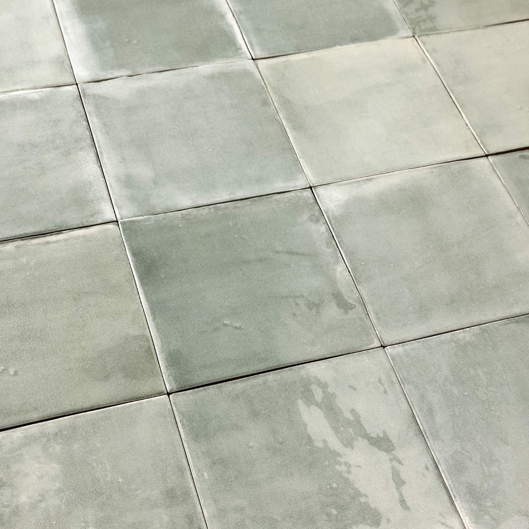 Angled ariel view of a group of glossy 5x5 textured light green blue earthy zellige tiles showing the textured edges and colour variation. 