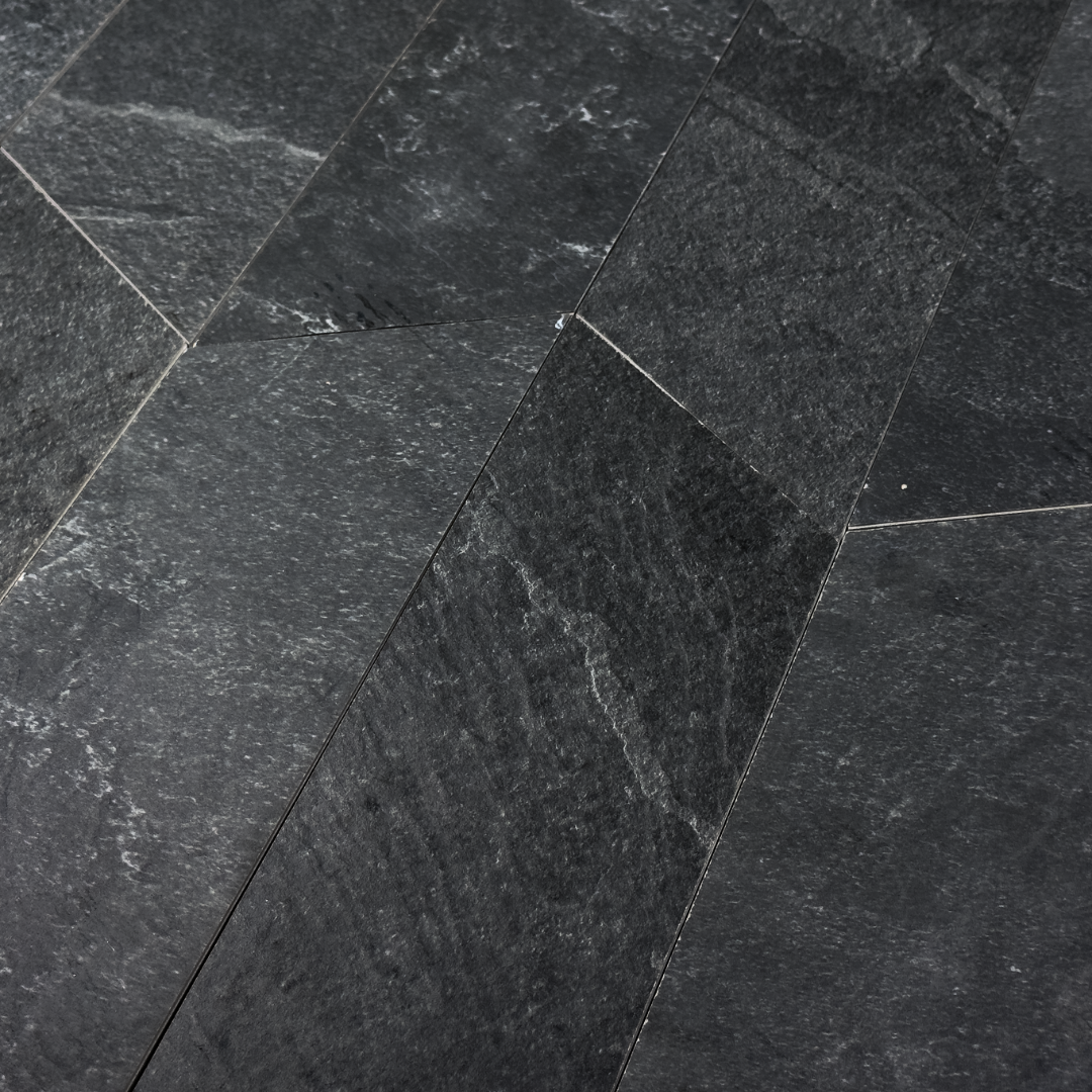 Angled close up view of a group of black slate look 4x20 chevron tiles to show the shape, colour and veining pattern. 