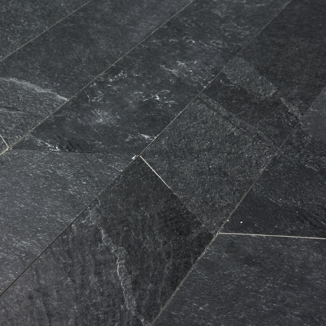 Angled close up view of a group of black slate look 4x20 chevron tiles to show the shape, colour and veining pattern. 