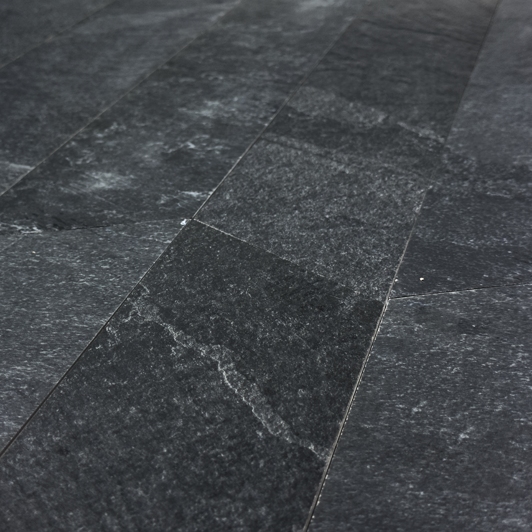 Angled close up view of a group of black slate look 4x20 chevron tiles to show where the edges meet, as well as highlighting the shape, colour and veining pattern. 