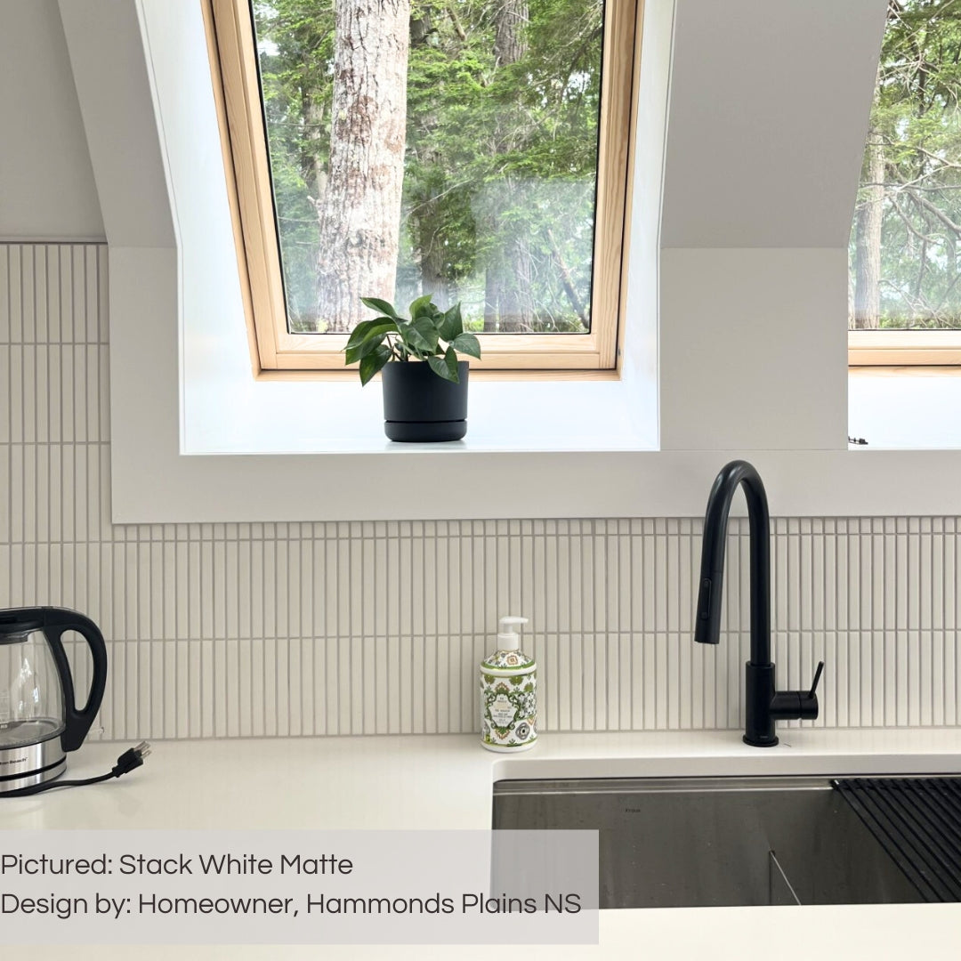A modern  white kitchen with bright light pouring in the windows. The backsplash tile is a white matte stacked kitkat mosaic. White countertop perfectly matches the tile. 