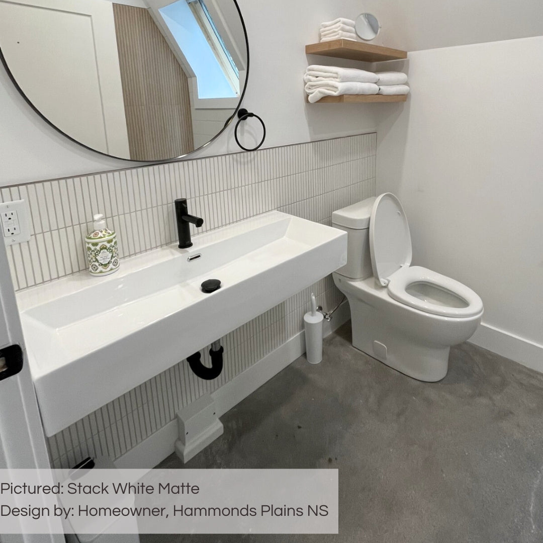 A minimalist washroom featuring white plumbing fixtures and a tiled backsplash. the tiles are white matte kitkat mosaics stacked vertically on the lower half of the wall. 