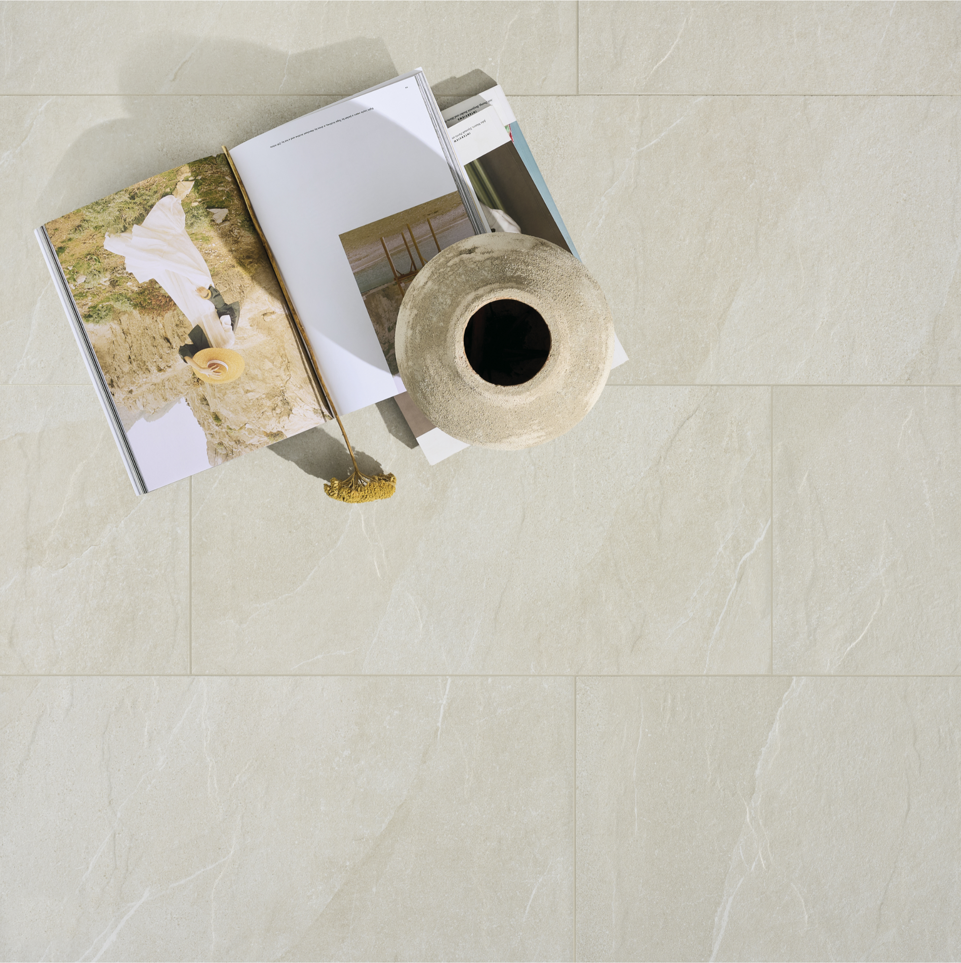 Ariel view of a floor installation of large 24x48 stonehaven light  tiles with very subtle and pretty veining pattern and a decorative clay vase resting on the floor. 