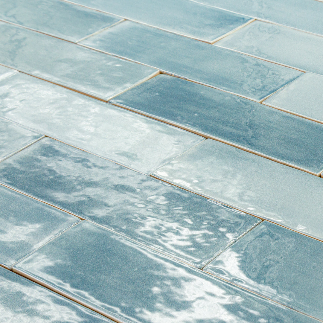 angled close up of a group of 2x6.5 glossy aqua azure blue subway tiles with colour variation in a brick layout