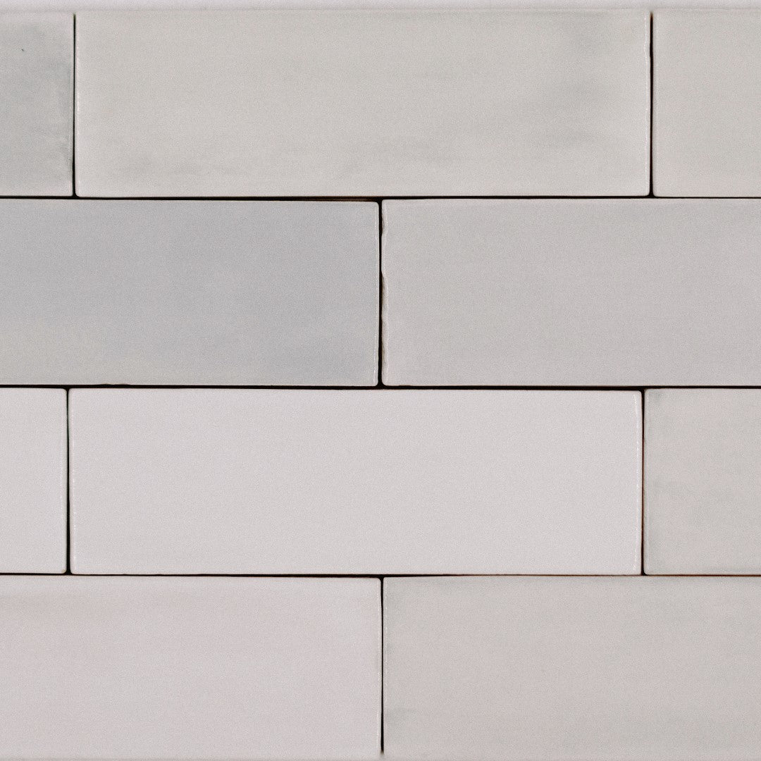 Ariel close up of a brick subway tile layout; the tiles are  2x6.5 glossy salt subway tiles in a warm grey light beige griege with heavy colour variation. 