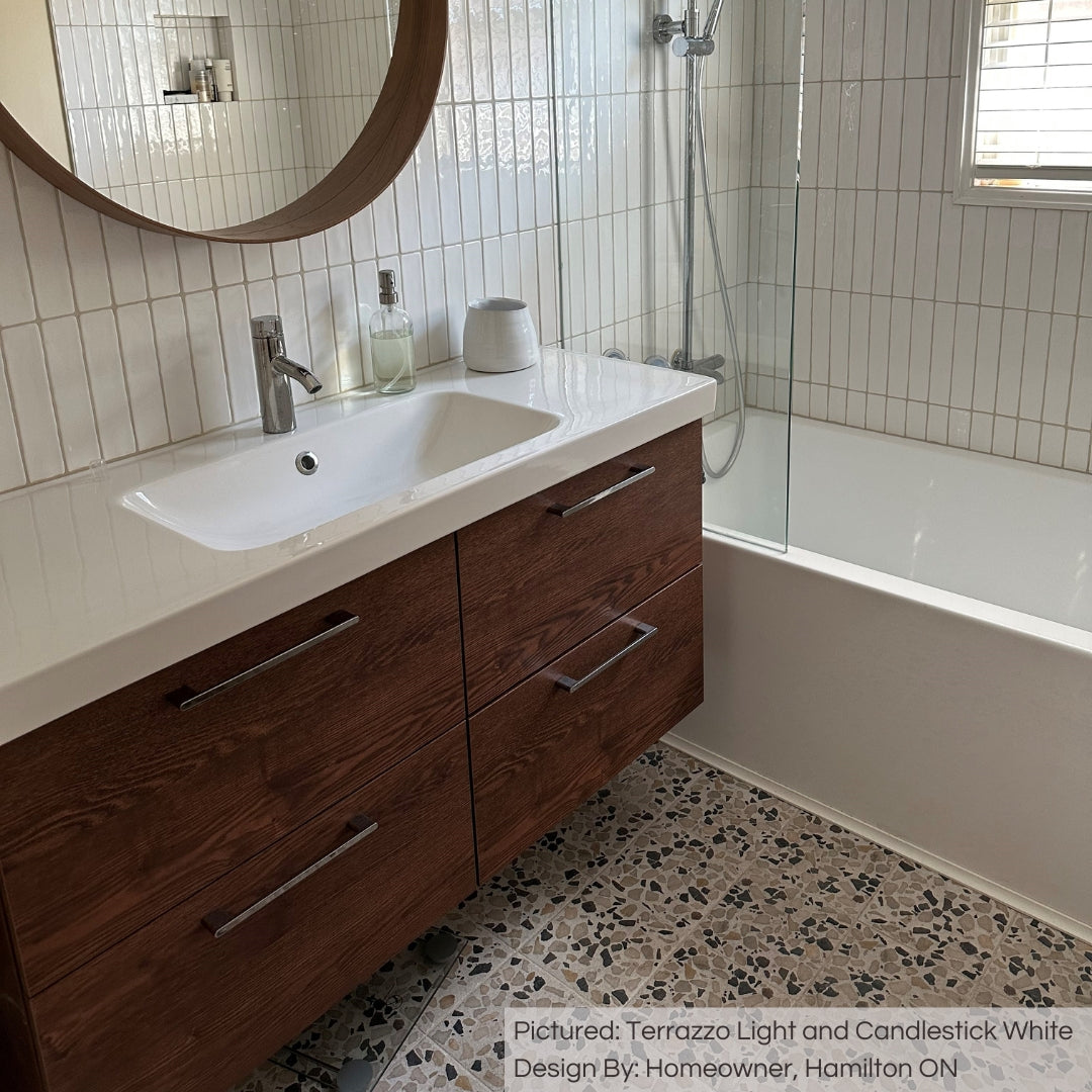 A natural vibe modern bathroom with terrazzo look tiles on the floor, wood accents and candlestick white 2x10 glossy tiles on the bathroom and shower walls installed in a vertical stack modern pattern. 
