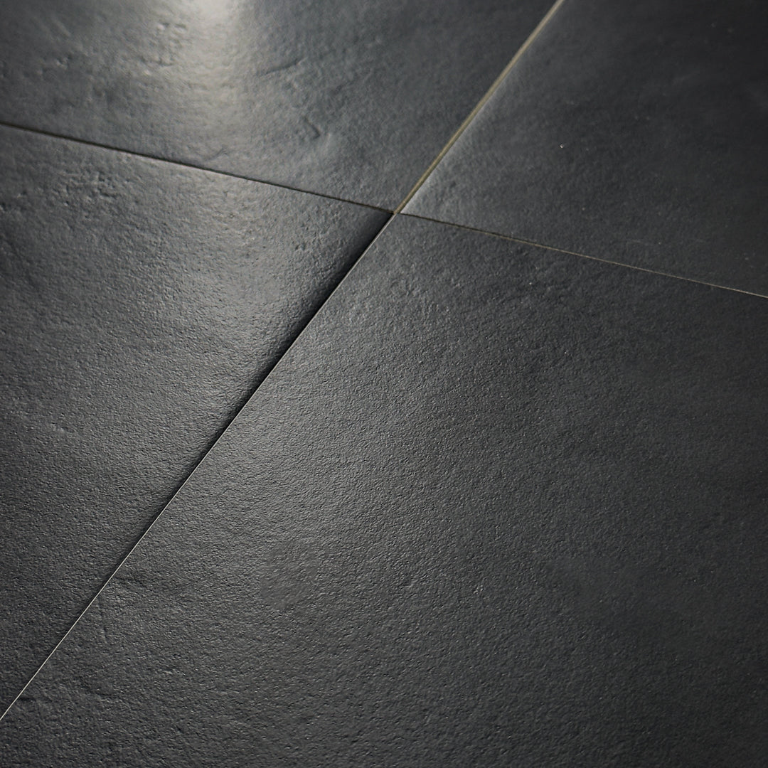 An angled close up view of four black 12x12 tiles together in a square. The tiles feature a stone look with subtle texture and a matte finish. 