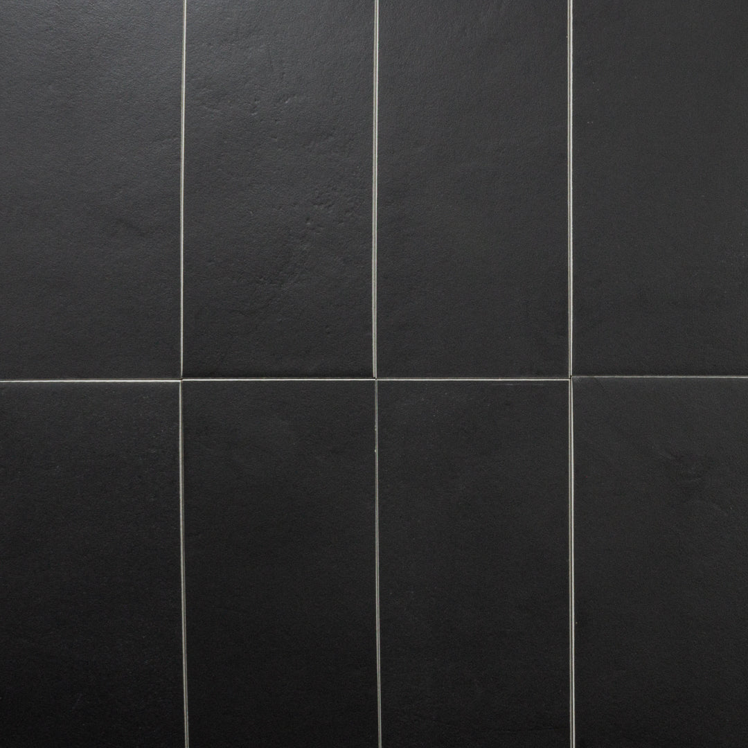 An ariel view of 8 tiles laid in a vertical stack pattern featuring black 4x12  with a soft stone appearance and texture. 
