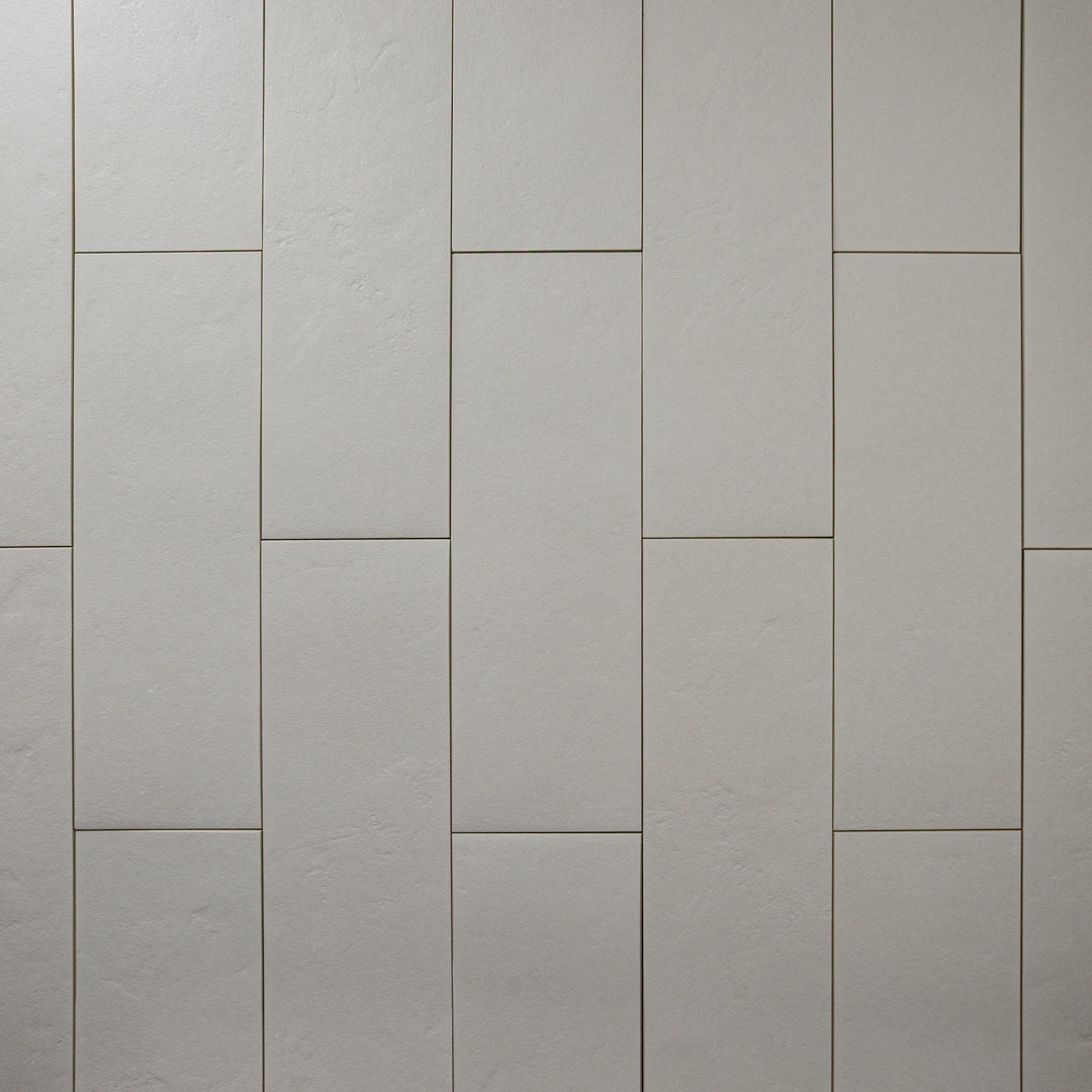 Multiple Grey 4x12 tiles laid out in a vertical brick pattern with a soft stone appearance and texture. 