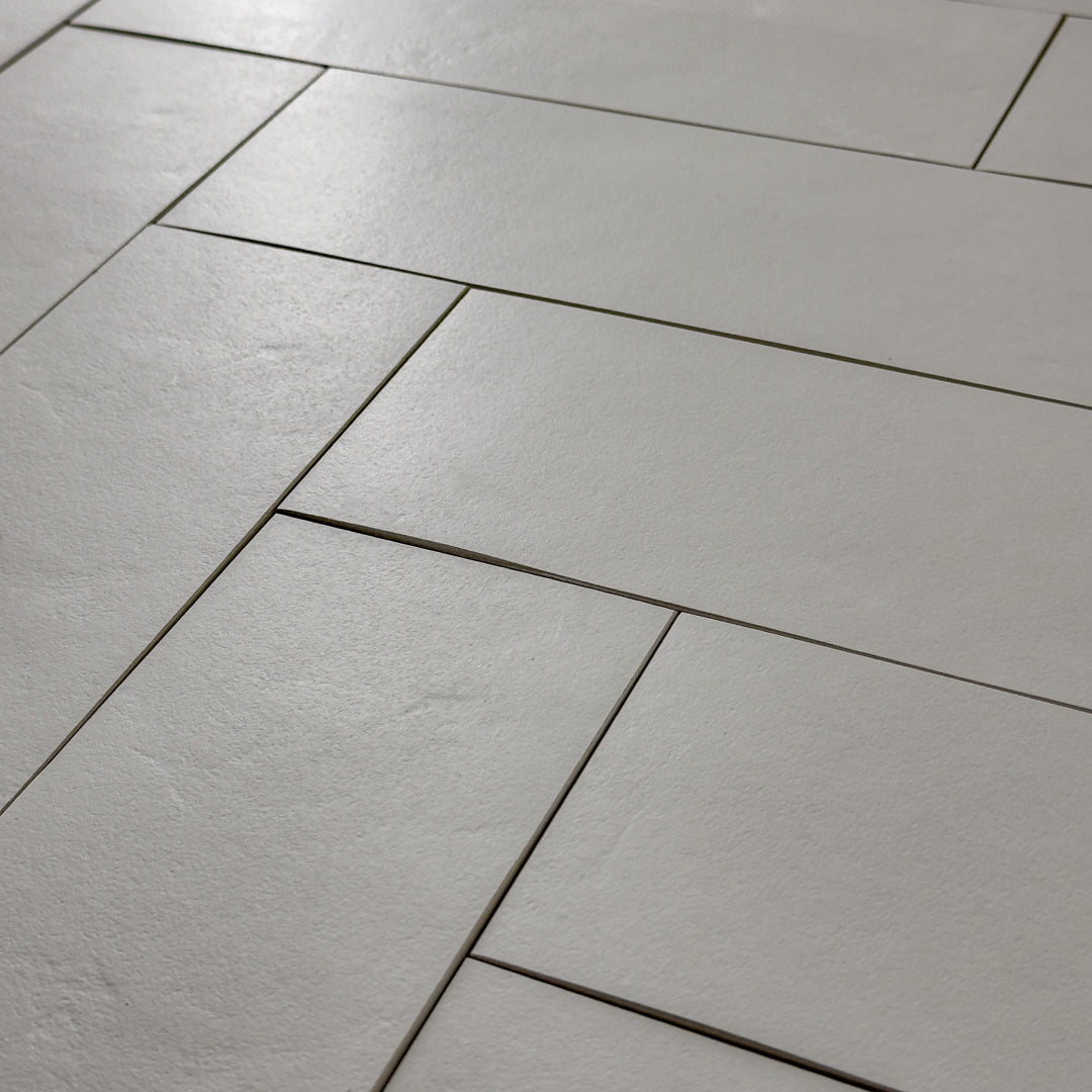 Close up view of Grey 4x12 tile laid out in a herringbone pattern to highlight the soft stone appearance and texture. 