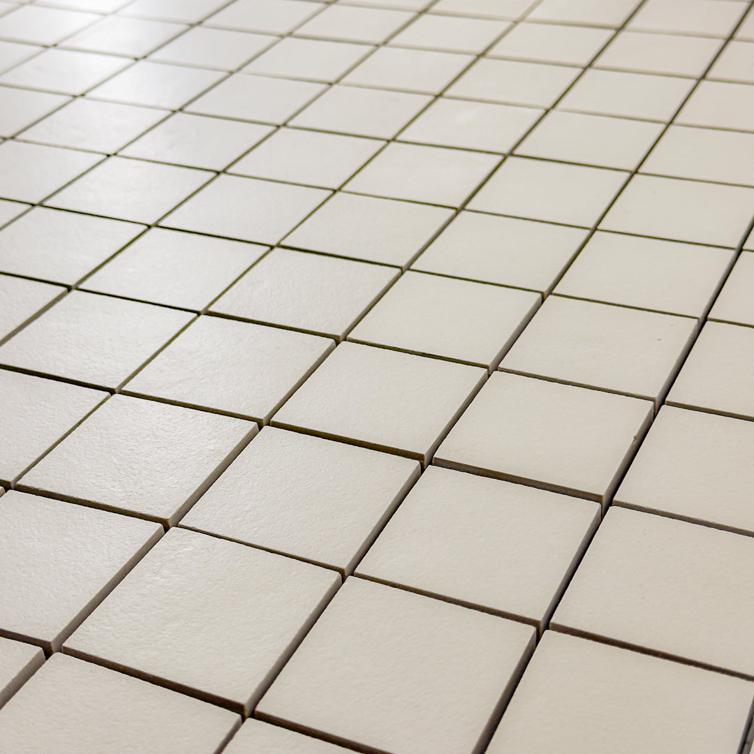 A close up detailed view of the 12x12 sheet mosaic tile made of 2x2 beige stone look tiles with a subtle texture