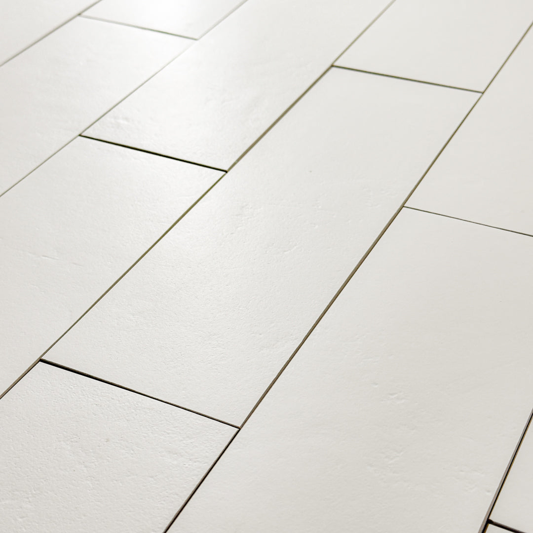 An angled close up view of multiple White 4x12 tiles laid out in a vertical brick pattern with a soft stone appearance and texture. 