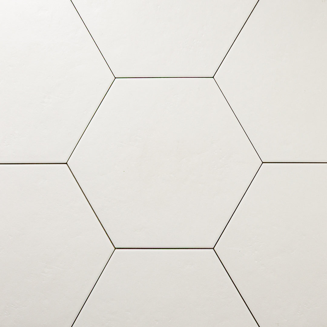 Close up view of seven white 9x10 hexagon tiles. There is one tile centered with six tiles surrounding it to form a honeycomb look. The checkmate white features a slight stone look, with subtle texture and a matte finish. 