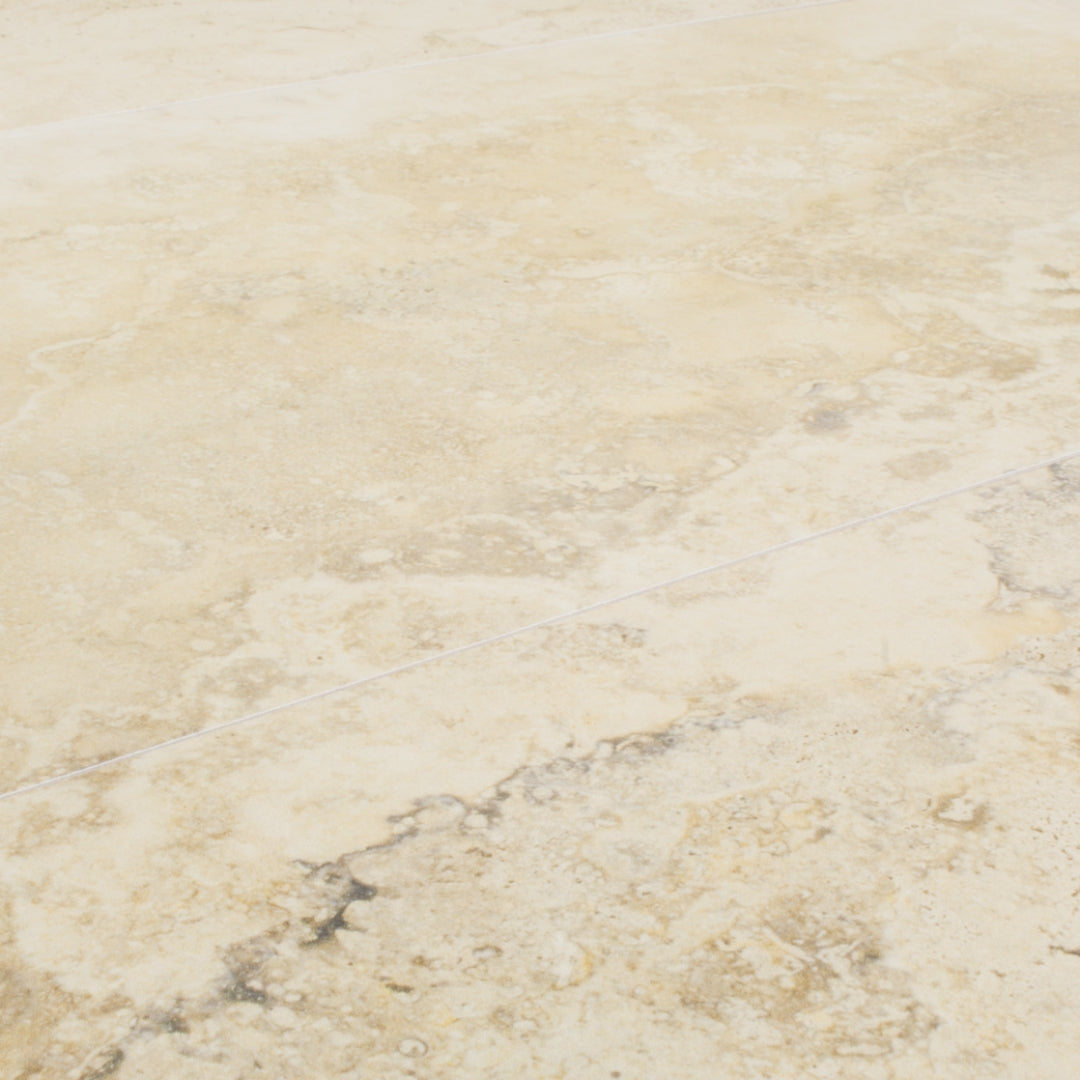 Angled close up view of two large rectangular tile that resembles travertine stone in light warm beige. 