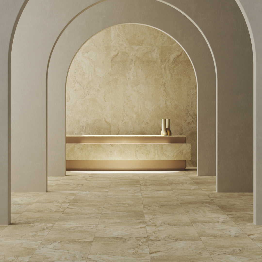 A commercial setting depicting an arched hallway leading to the a reception desk. The floor, wall behind the desk and face of the desk are covered in a porcelain tile that is warm travertine stone looking. The other neutral tones on the painted walls and decor compliment eachother. 