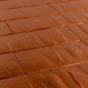 Angled close up view of 3x12 pumpkin orange textured tiles arranged in a brick layout. 
