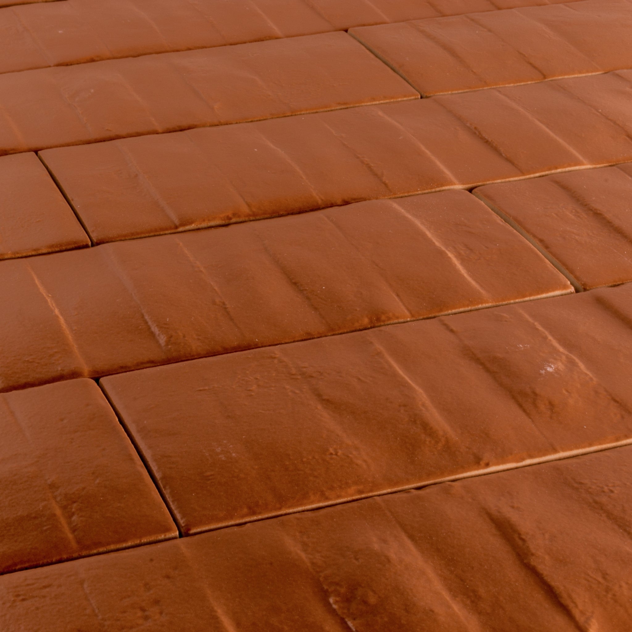 Angled close up view of 3x12 pumpkin orange textured tiles arranged in a brick layout. 