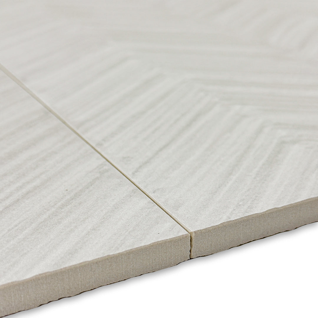 angled close up of the edge of two chevron pattern solenne grey structured tiles. 