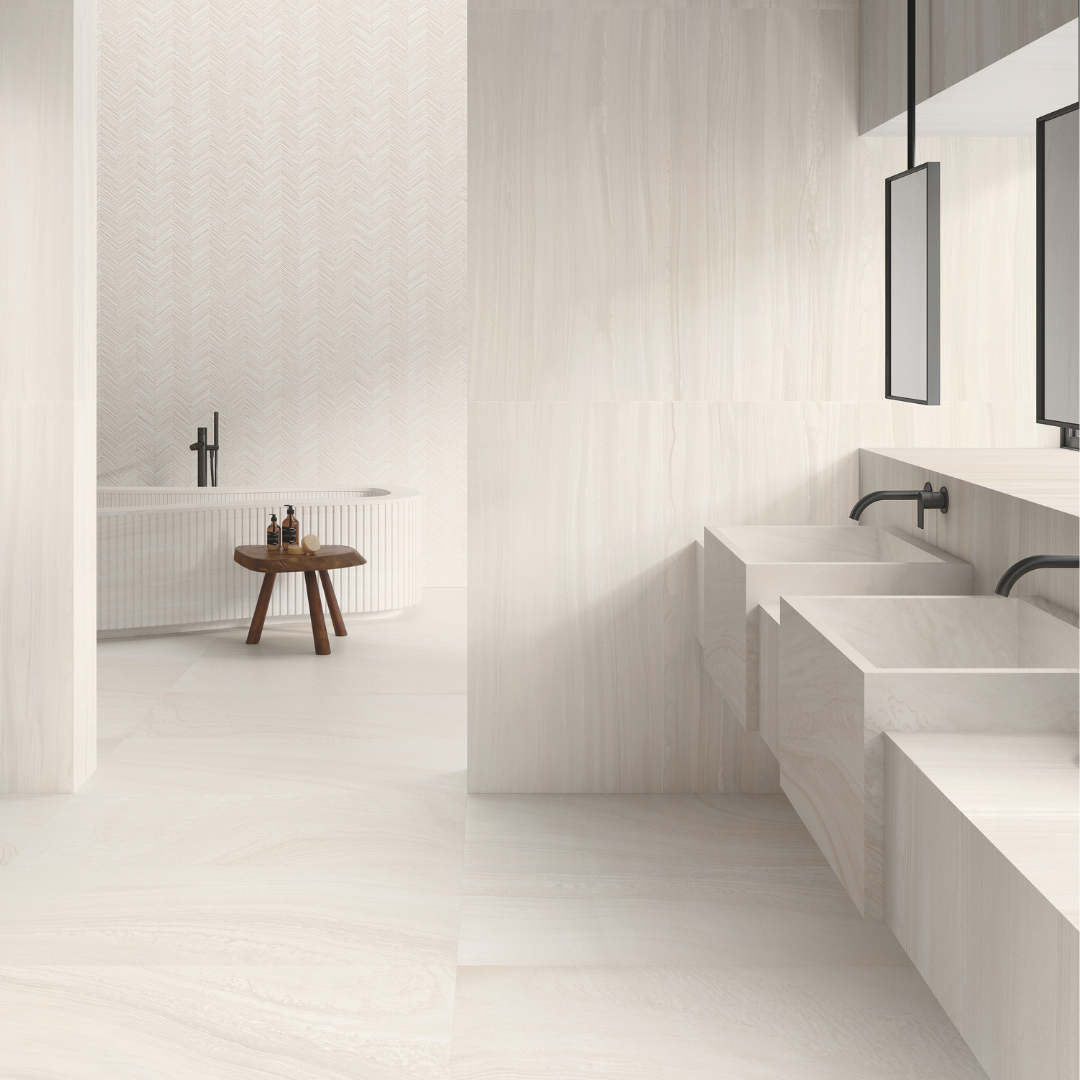 Doorway view of a modern but minimalistic ensuite with two  stone wall mounted vanities and a standalone bathtub. the floors and most of the walls are covered in tilesinspired solenne white stone look tiles and the focal wall behind the bathtub is the structured version that is the same stone look but has a chevron pattern carved into the tiles giving a visual texture. 