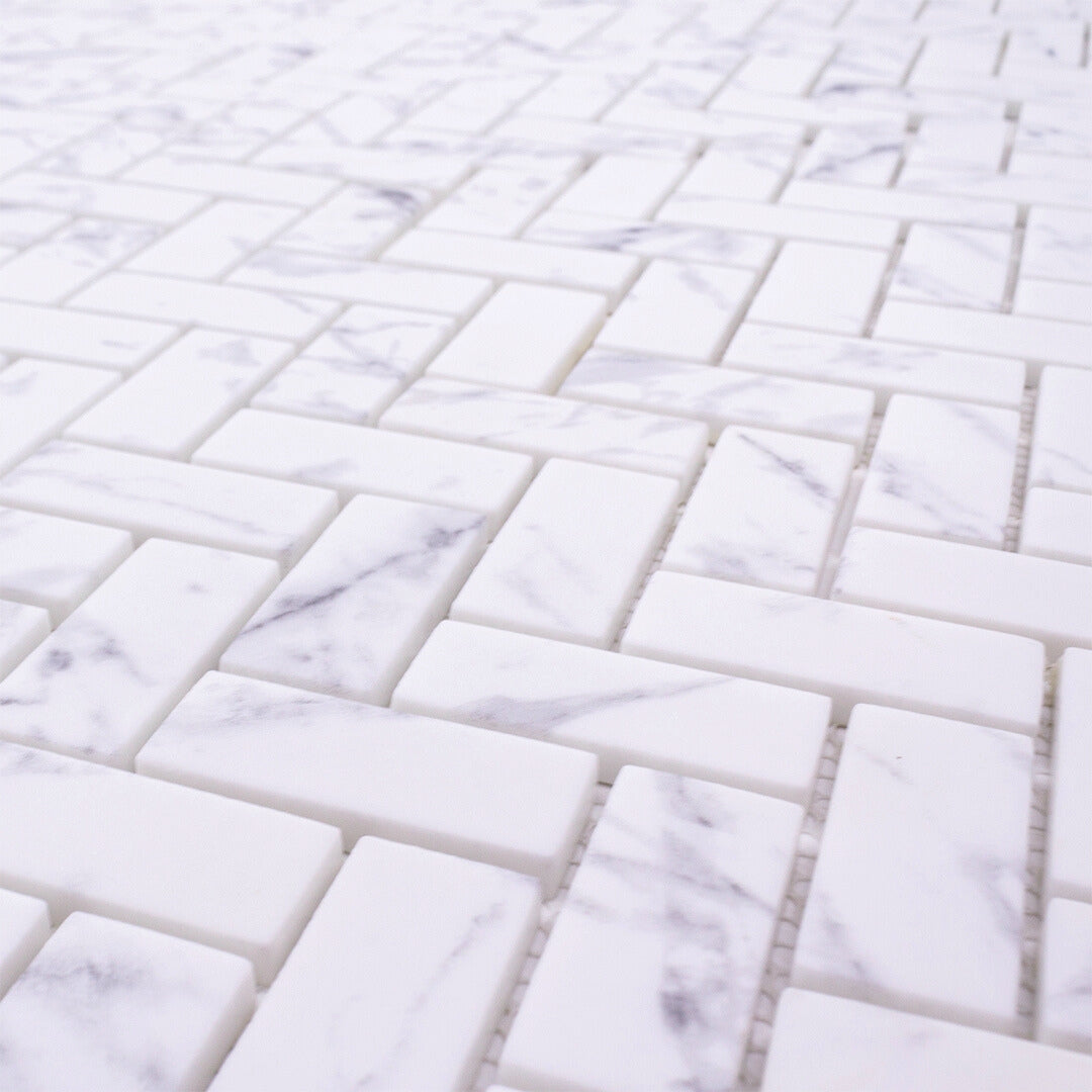 Close up view of herringbone mosaic tiles the tiles are white and have a grey marble veining pattern. 