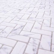 Close up view of herringbone mosaic tiles the tiles are white and have a grey marble veining pattern. 