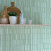 A close up of a kitchen or panty tiled backsplash with open shelving. the tile is a fluted green kitkat style 4.5x9 tiles in a matte finish. there are light shades of green in the variation. 