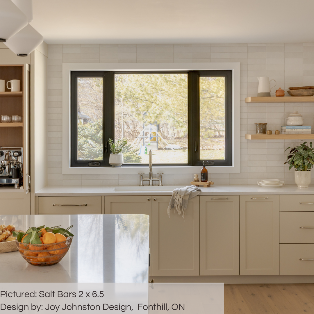 An airy and cozy kitchen with light wood accents and a tile backsplash. the tiles are 2x6.5 glossy salt subway tiles in a warm grey light beige griege with heavy colour variation. 