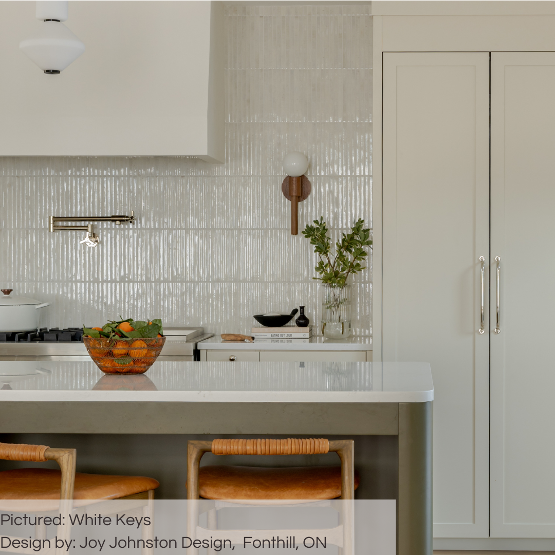 A beautiful transitional kitchen with white cabinets, white counters and a olive green island with rattan accents. The tiled backsplash adorns the entire wall where the stove is and the tiles catch the light in a captivating way. The tiles are 5x10 panels in glossy milk white, the tile has a 3D linear faux grout line kitkat look and colour variation. 