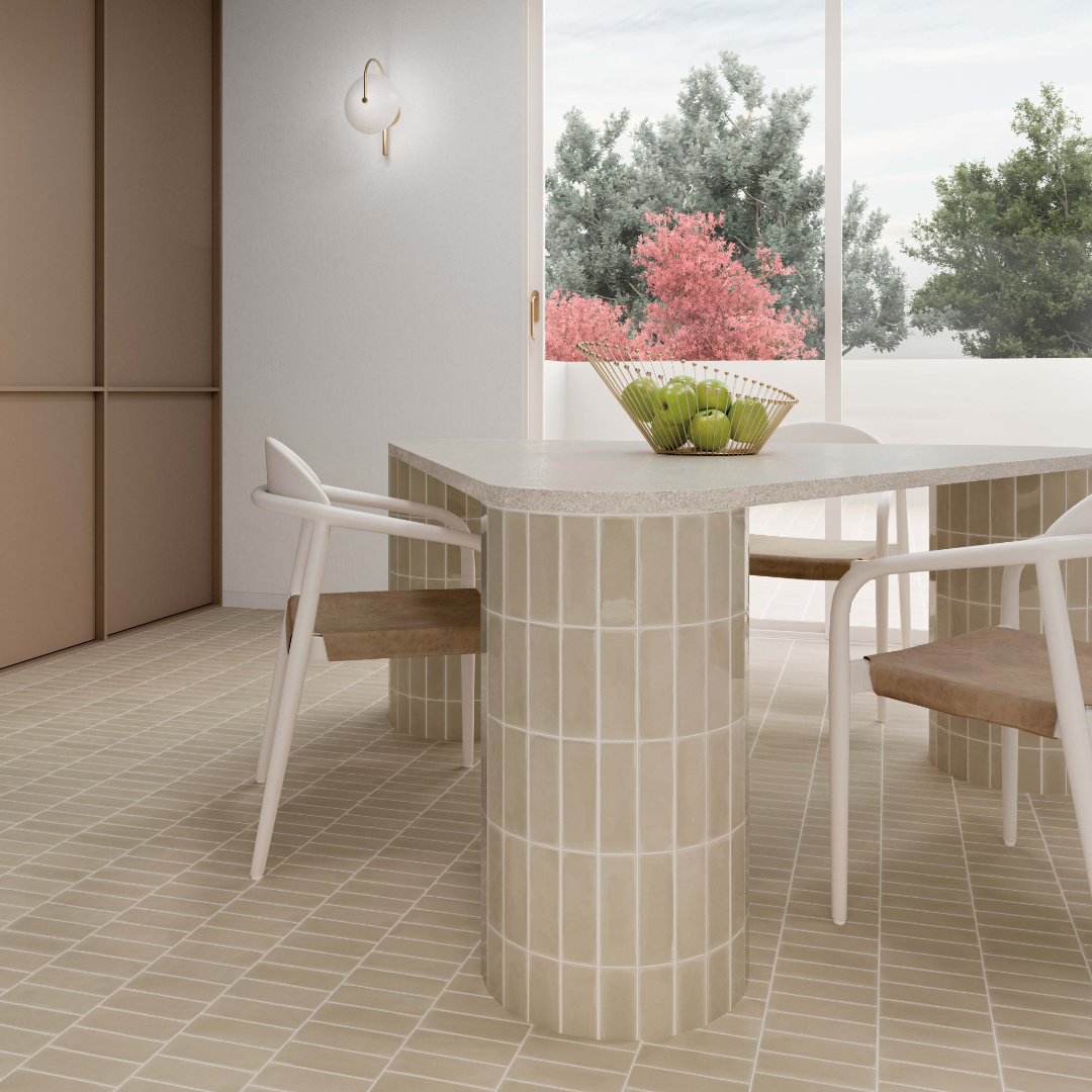 A modern Scandinavian dining area with a taupe beige matte subway tile on the floor and on the round cylinder legs of the table in a vertical stack. 