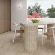 A modern Scandinavian dining area with a taupe beige matte subway tile on the floor and on the round cylinder legs of the table in a vertical stack. 