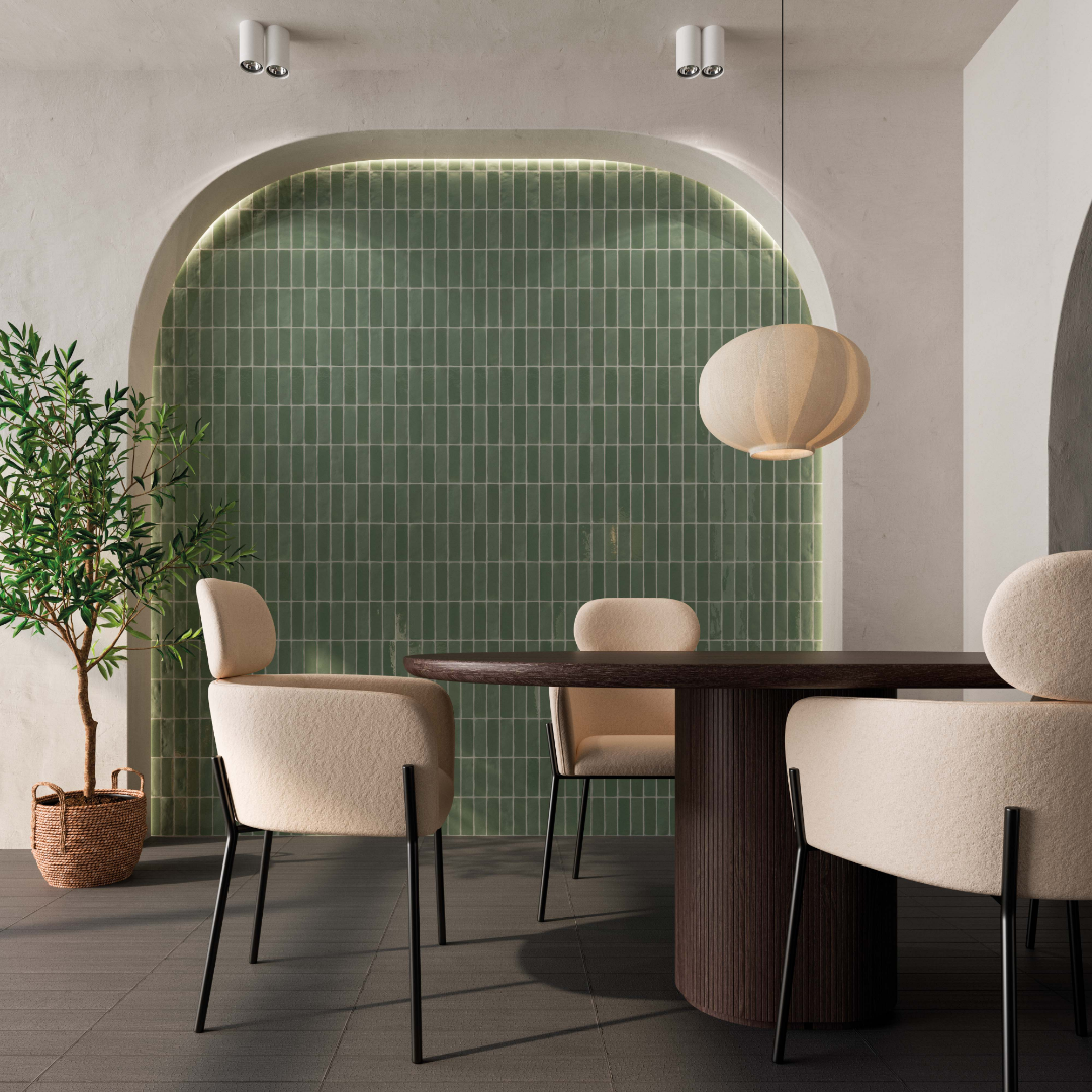 A modern dining space with cream and dark wood dining table and seats. The backdrop beyond a carved arch is a green 2x6 woodland fir glossy green tile with subtle colour variance. 