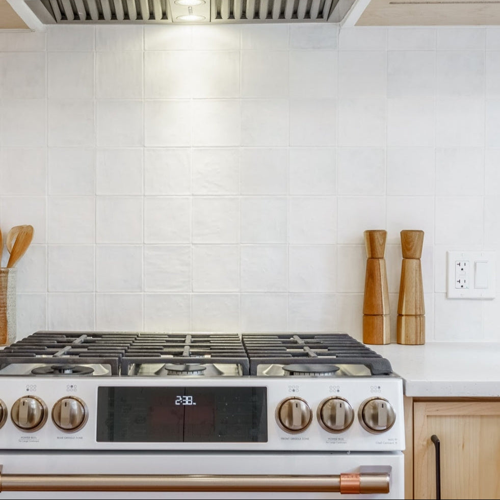 A close up of a modern range with zellige powder matte textured handmade look tiles installed on the backsplash. 