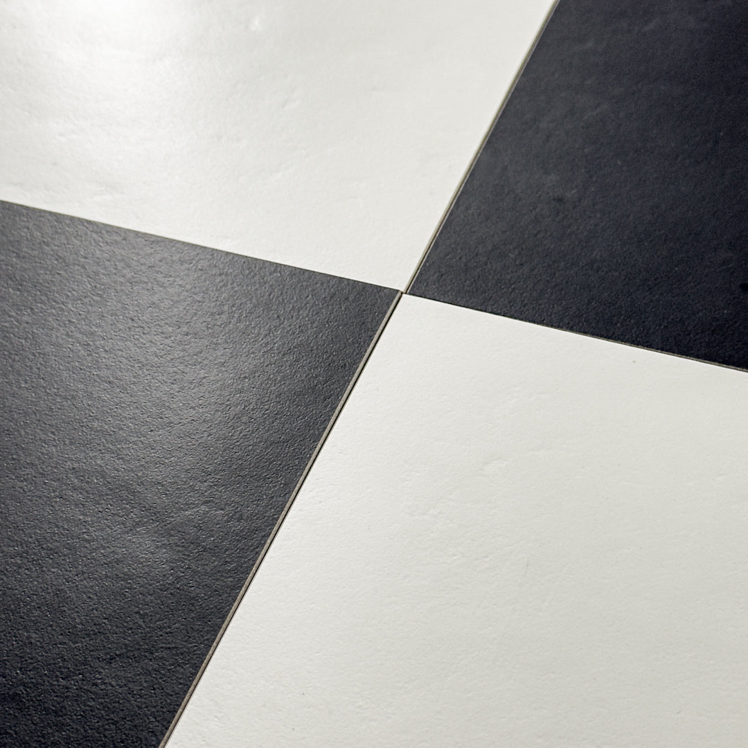 Angled close up view of 2 white and 2 black tiles laid in a checkerboard pattern. Checkmate White 12x12 and Checkmate Black 12x12, these two tiles feature a slight stone look, with subtle texture and a matte finish. 