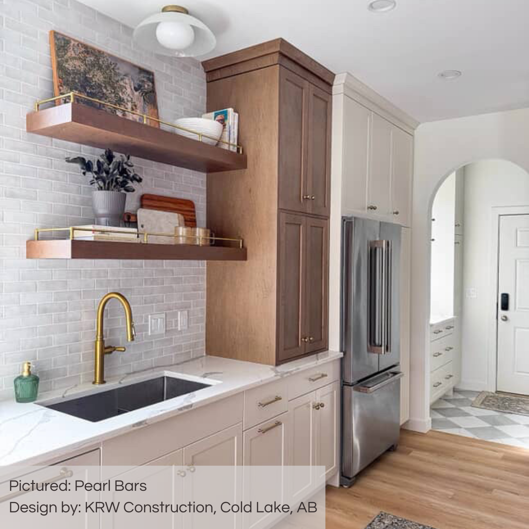 A delightful and bright kitchen with white fixtures and some wood shelving and closed cabinetry in wood and white. from this angled perspective we are seeing the wall backsplash that have been tiled with pearl bars variated off white subway tiles in a traditional brick layout. 