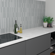 a modern kitchen with dark grey cabinets, white countertops and a fluted cool blue grey tile backsplash. the tiles are viva ash by tilesinspired