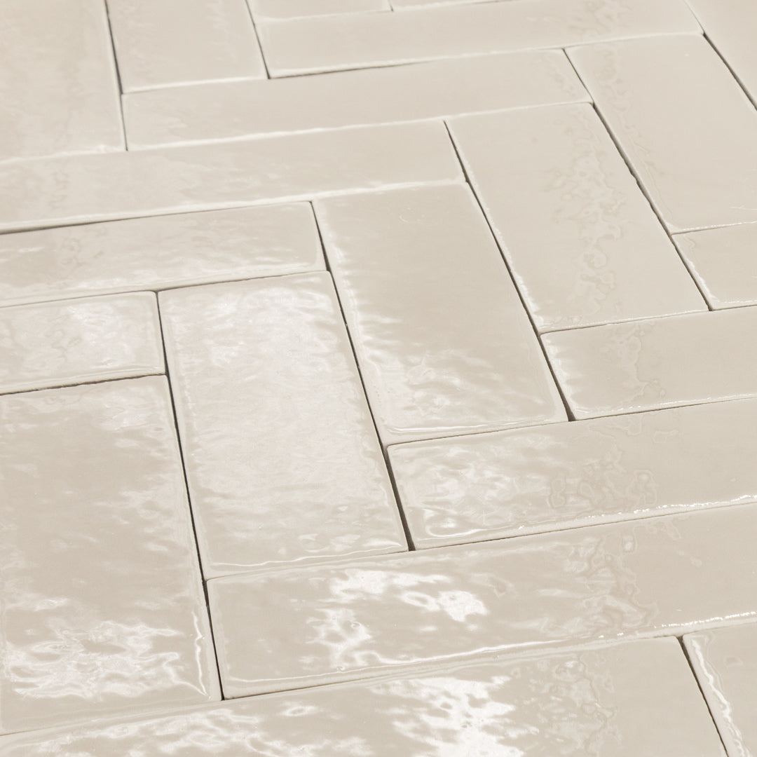A group of 2x6 glossy beige subway tiles laid out in a herringbone pattern. the finish catches the light along with the subtle texture of the tiles. 