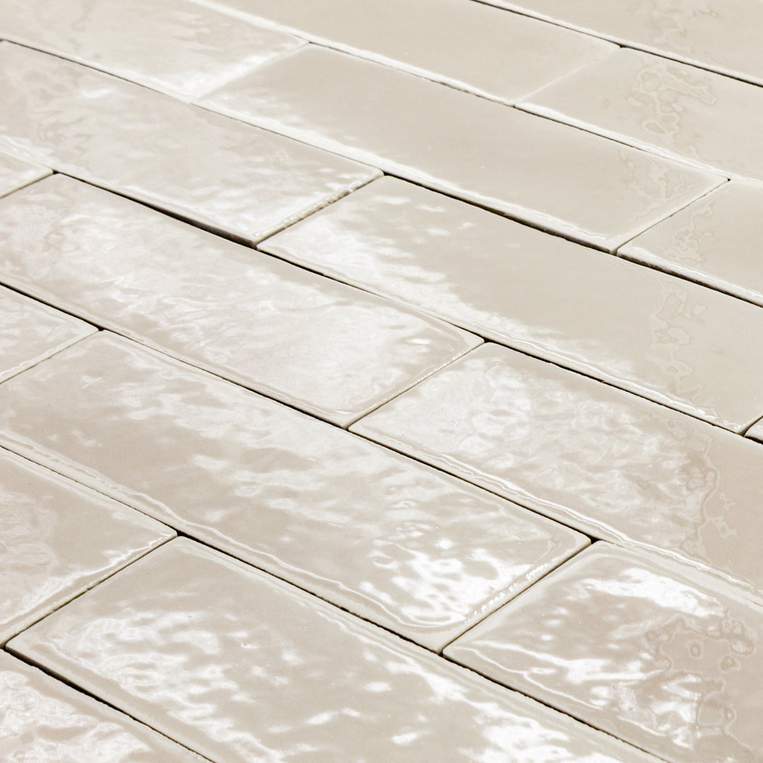 angled view of a group of beige 2x6 glossy subway tiles laid out in a brick pattern to highlight the texture. 