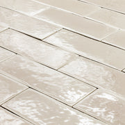 angled view of a group of beige 2x6 glossy subway tiles laid out in a brick pattern to highlight the texture. 