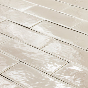 angled view of a group of beige 2x6 glossy subway tiles laid out in a brick pattern to highlight the texture. 