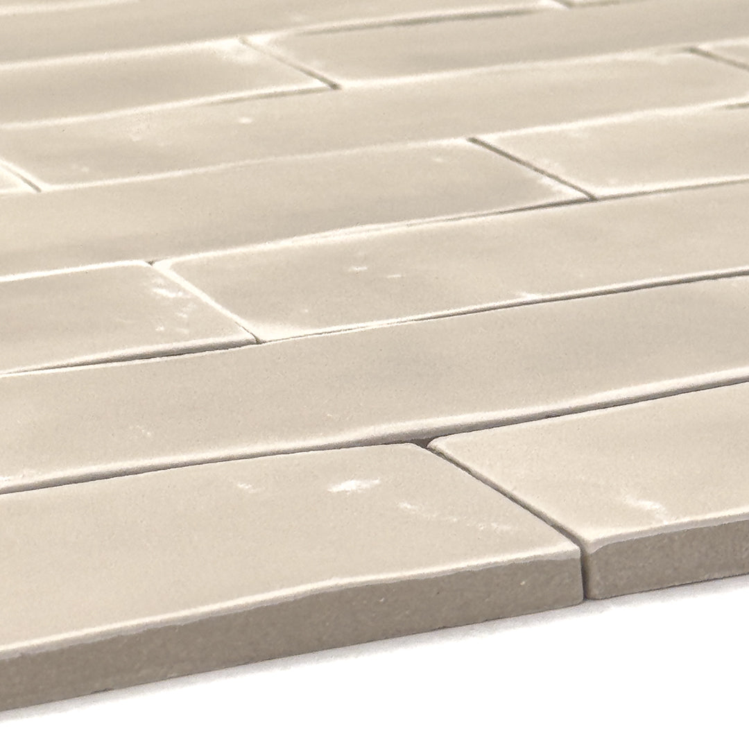 angled close up of a group of beige 2x6 matte subway tiles with a soft texture and variance in a brick layout. this angle highlights the texture of the edges. 