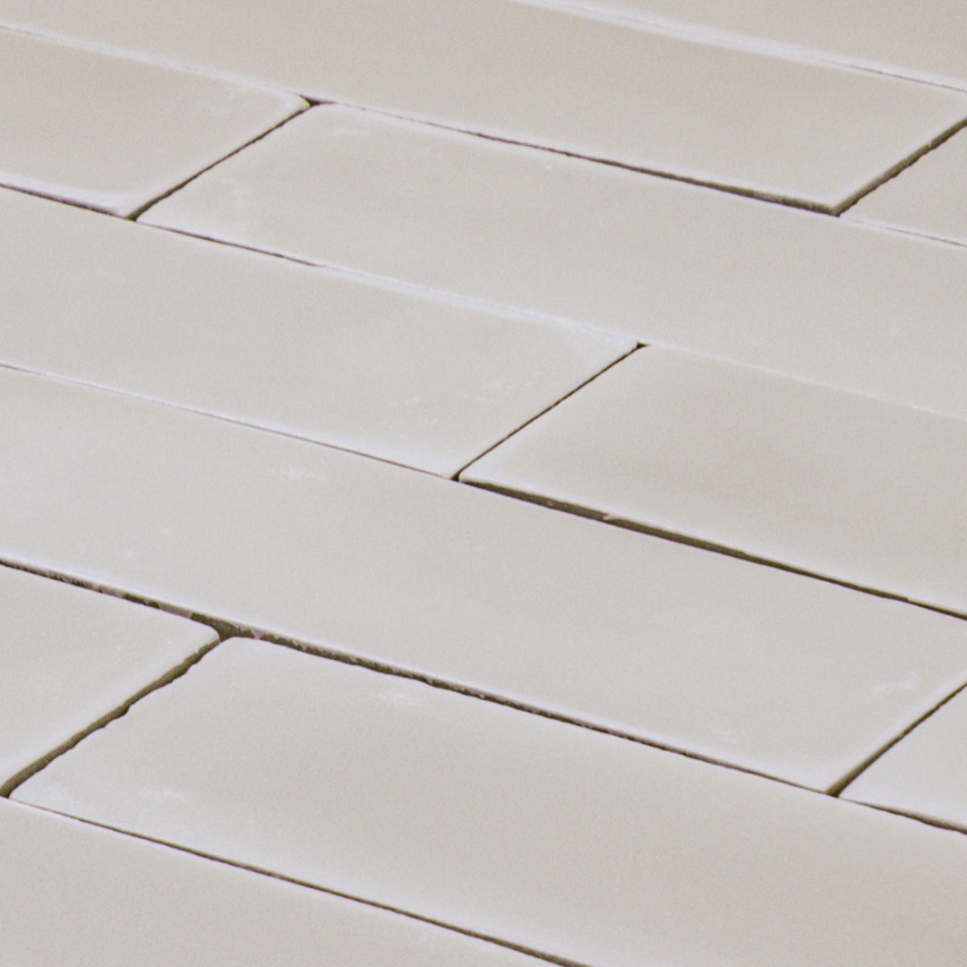 a group of taupe 2x6 matte subway tiles with a soft texture and variance in a brick layout shown on an angle to highlight the uneven texture of the tile edges. 
