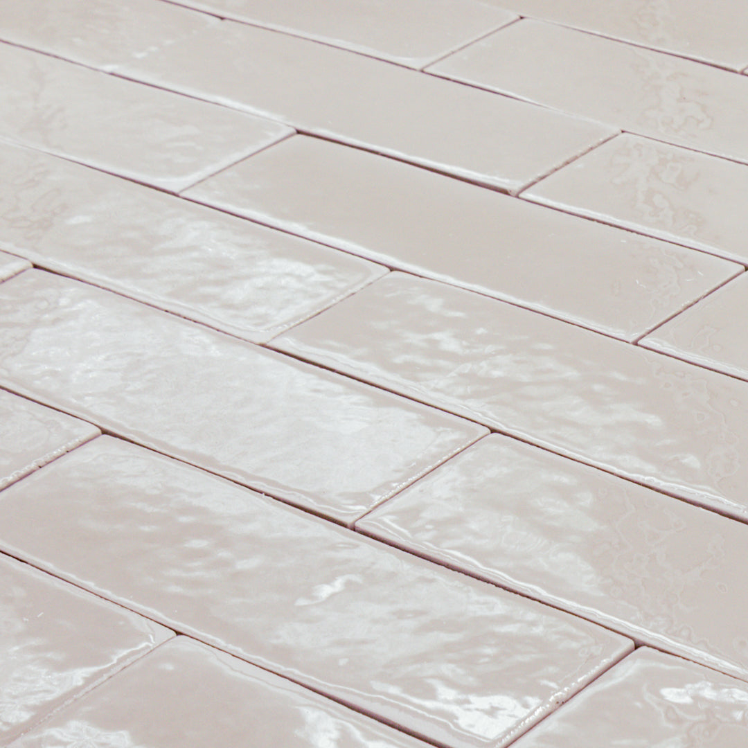 a group of taupe 2x6 glossy subway tiles with a soft texture and variance in a brick layout at an angle to highlight the uneven edges of the tiles for texture. 