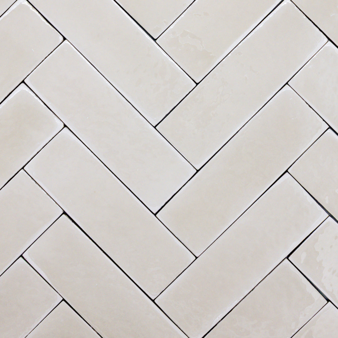 a group of taupe 2x6 glossy subway tiles with a soft texture and variance in a herringbone layout. 