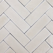 a group of taupe 2x6 glossy subway tiles with a soft texture and variance in a herringbone layout. 