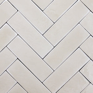 a group of taupe 2x6 glossy subway tiles with a soft texture and variance in a herringbone layout. 