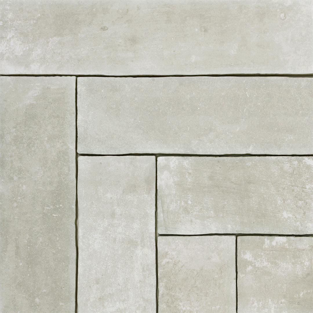 A group of 11x2.75 brick clay silver cement grey stone look tile focused on the herringbone pattern where the tiles meet with a natural looking edge
