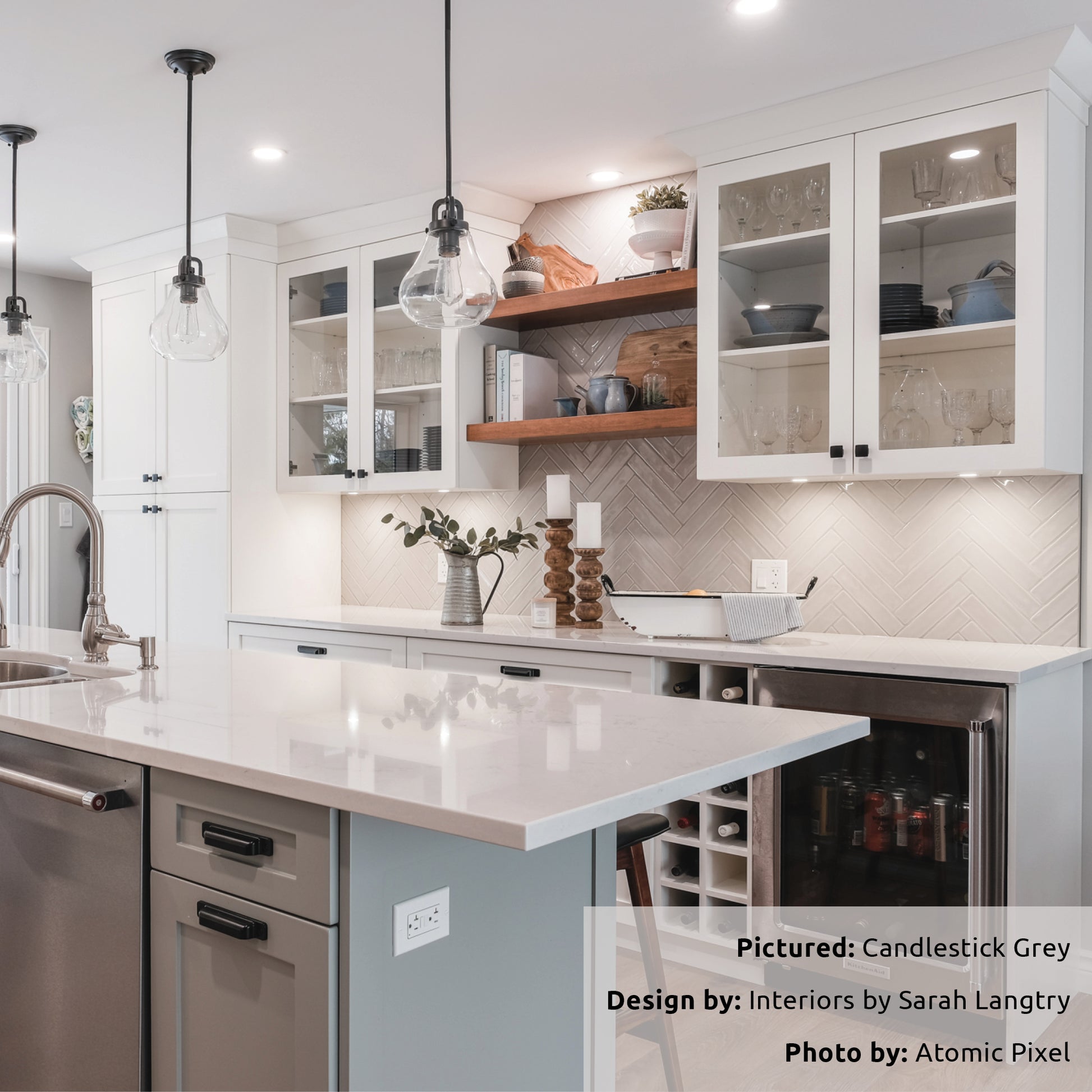 A modern white and grey kitchen with wood open shelves above the bar area and the backsplash is tiled in candlestick grey 2x10 glossy laid in a herringbone pattern. 