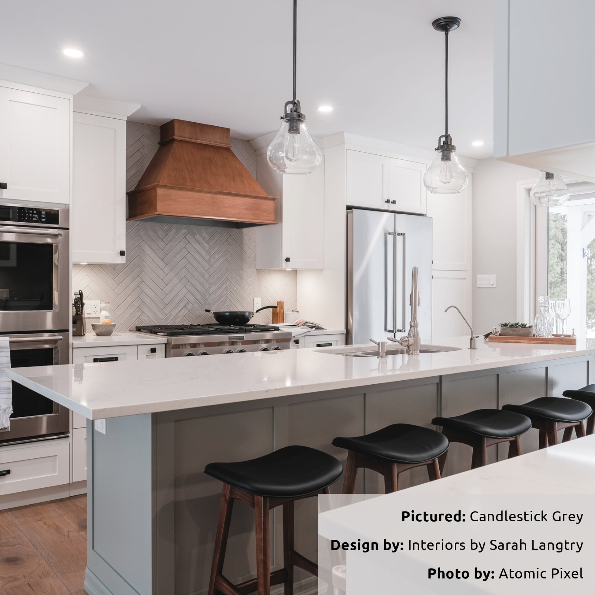 A neutral white kitchen with a wood grain range hood, this compliments the candlestick grey 2x10 glossy tiles installed in a herringbone pattern on the backsplash. 